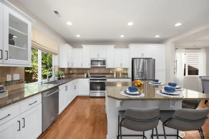 The chef’s kitchen featuring granite countertops, full_height backsplash, designer cabinetry with glass inserts and under cabinet lighting.