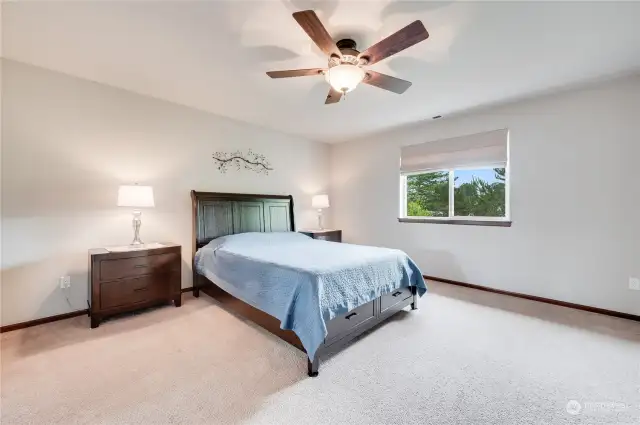 Spacious primary bedroom features ceiling fan and peek view of the Cascade Mountains