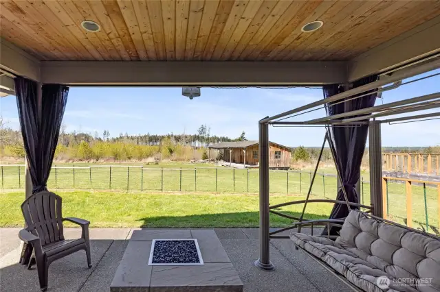Drapery-style shades surround the covered patio, creating a cozy outdoor living space. A custom dog-safe fence encloses the area.