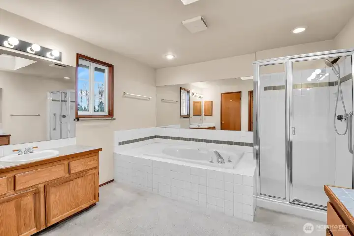 Spacious primary bath has generous soaking tub, separate shower, skylight, and two vanities, each with its own sink and cabinetry.