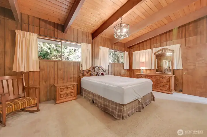 The primary bedroom on the main has warm vaulted wood ceilings and windows that are slightly higher than usual for privacy. The curtains on the right side actually hide a ply-wood space, I'm unsure why - perhaps a window was there in the past.