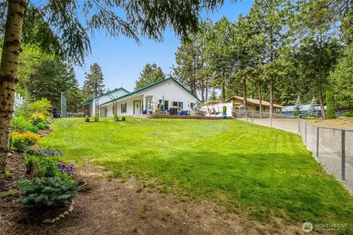 Rear exterior of home with large lawn, fencing, and shop in background