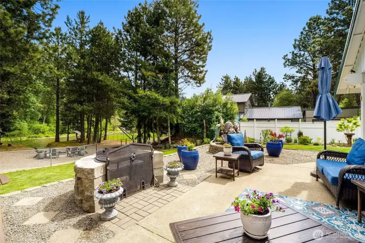 Backyard patio with fire feature, seating, and landscaped yard with tree coverage