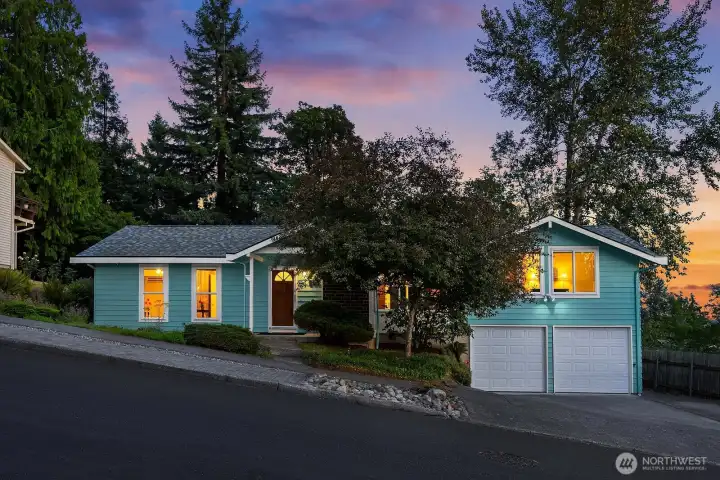 Beautifully maintained and warmly illuminated at sunset, the home showcases its fresh exterior paint, 50-year roof, mature landscaping, and two-car garage.