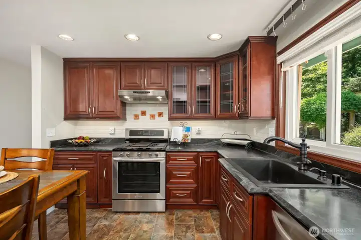 The kitchen features a gas range, expansive counters, a tiled backsplash, deep sink, and cabinetry designed to maximize storage.
