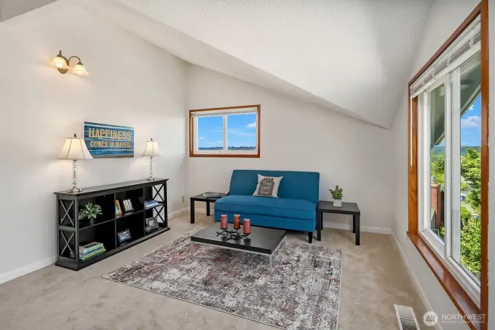 A comfortable bedroom with a vaulted ceiling, soft carpeting, and a triple-pane window capturing natural light and distant views.