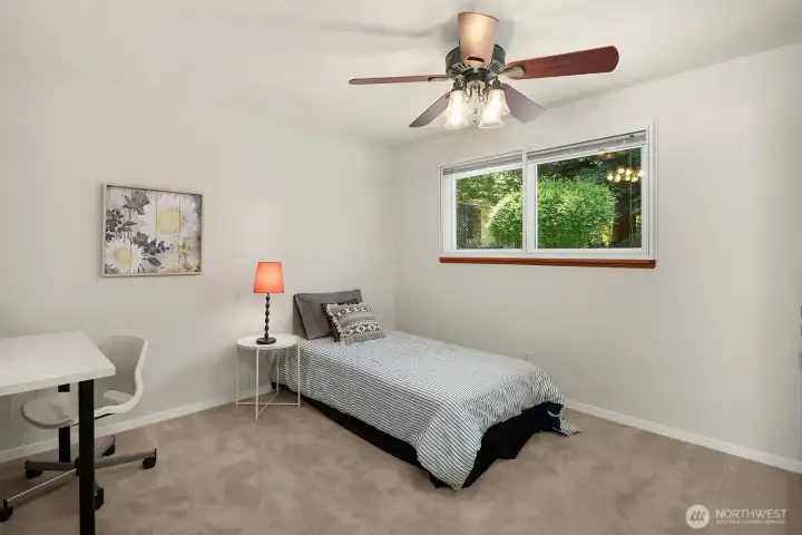This spacious bedroom offers generous floor space, a ceiling fan, and a triple-pane window with a peaceful view of the greenery outside.
