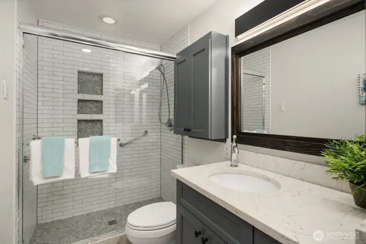 Beautifully renovated with a walk-in-style shower, sliding glass doors, elegant tile finishes, multiple recessed niches, and a contemporary vanity.