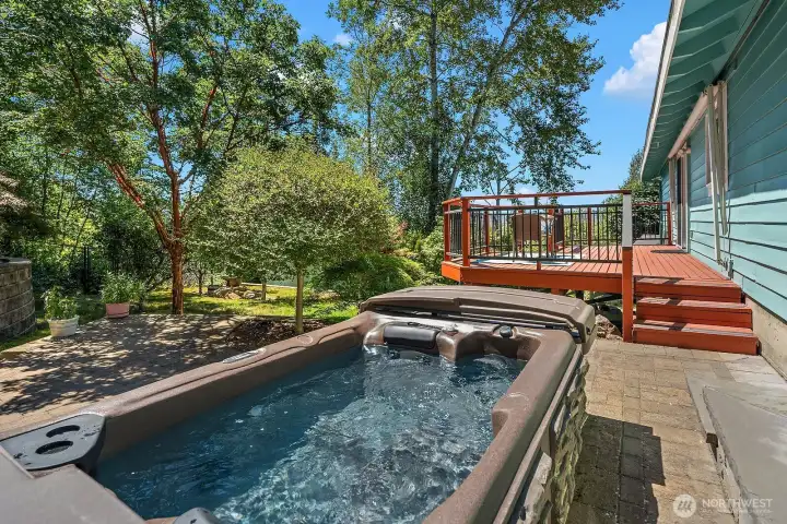 A system-paver patio creates a dedicated outdoor retreat with space for a hot tub, seating, and easy access to the elevated deck.