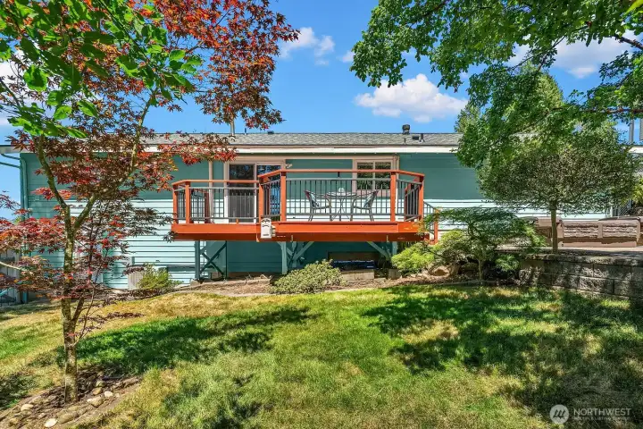 The backyard offers a comfortable balance of lawn, established trees, landscaped terraces, and an elevated deck for outdoor dining and relaxation.