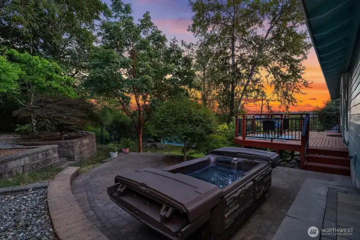 A system-paver patio creates a private outdoor retreat with a hot tub, mature landscaping, and colorful evening views.