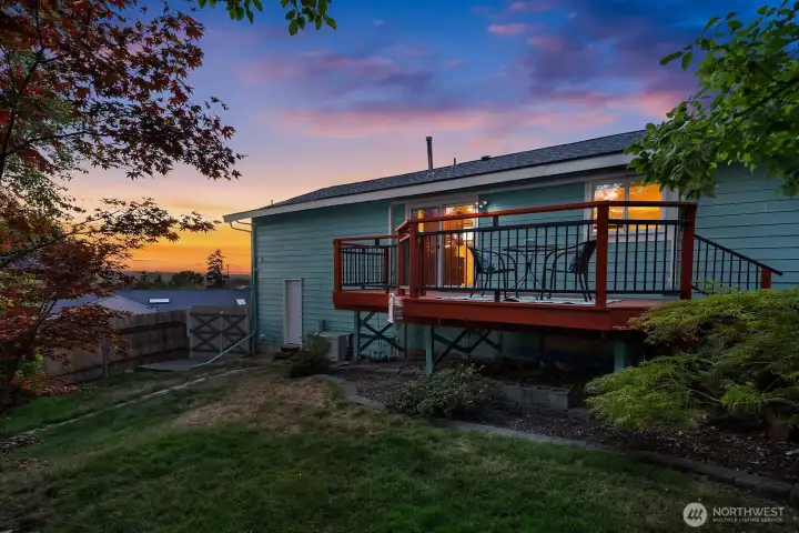 Mature Japanese maples and layered landscaping frame the rear deck and fully fenced backyard as the evening light settles in.