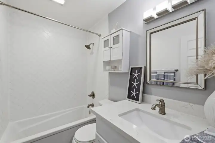 View of bathroom with single vanity, tub, shower with herringbone tile design and toilet