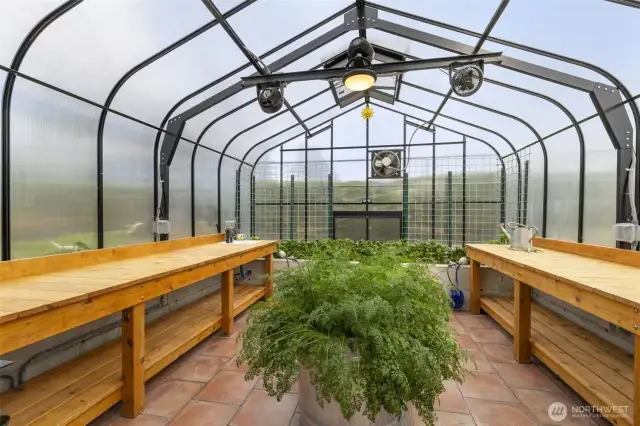Interior of greenhouse showcasing tile floors, rasied beds and potting bences.
