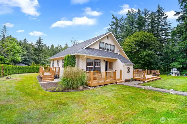 Quaint and beautifully maintained home surrounded by mature trees, featuring an expansive deck, a partially fenced yard, and plenty of space for outdoor entertaining