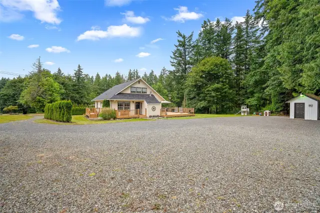 Spacious gravel driveway leads to this charming home with expansive deck space, detached storage shed, and a generous backyard surrounded by lush evergreens—perfect for privacy and outdoor living.