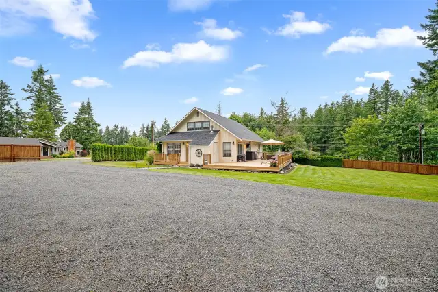 Charming home with expansive deck and large gravel parking area—set on a spacious, fenced lot surrounded by evergreens for privacy and peaceful outdoor enjoyment.
