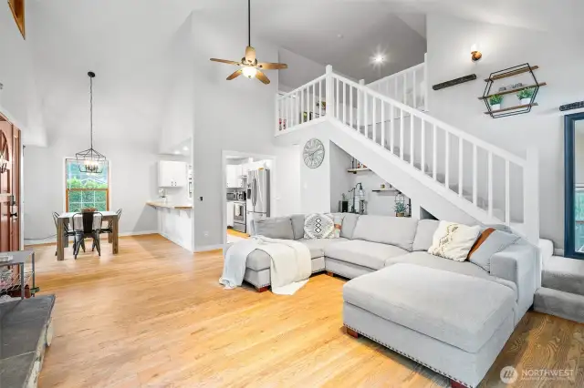 Beautiful open-concept living space with soaring ceilings, hardwood floors, and a modern staircase leading to the loft—seamlessly connecting the living, dining, and kitchen areas for effortless flow and comfort.