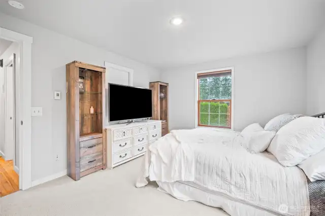 Spacious primary bedroom with soft carpeting, large windows, and stylish built-ins—perfect for relaxing in comfort with natural light and privacy.