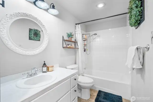 Charming full bathroom featuring a classic white vanity, tile shower/tub combo, and stylish accents for a clean, inviting feel.