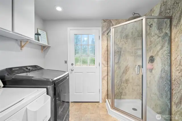 Multifunctional laundry room featuring built-in cabinetry and a beautifully tiled walk-in shower with direct outdoor access.