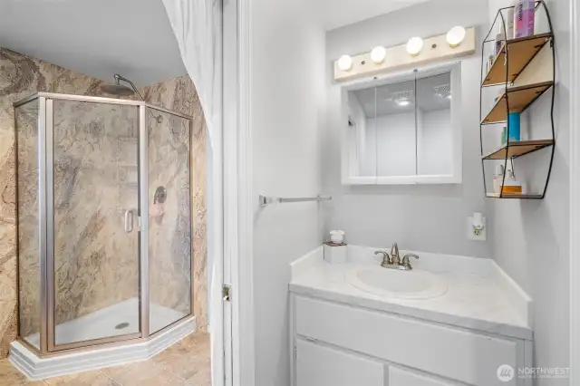 Bright and functional bathroom featuring a classic white vanity, mirrored medicine cabinet, and a beautifully tiled walk-in shower with glass enclosure