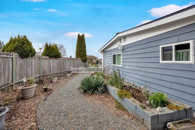 Side yard has gravel walking path. Raised garden bed for herbs, vegies etc. Gardners delight!
