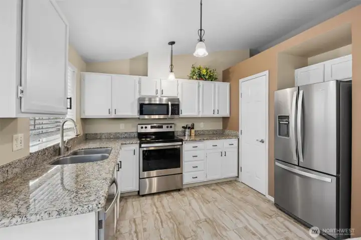 Updated kitchen featuring white cabinetry, stainless steel appliances, a walk-in pantry, granite countertops, and backyard views.