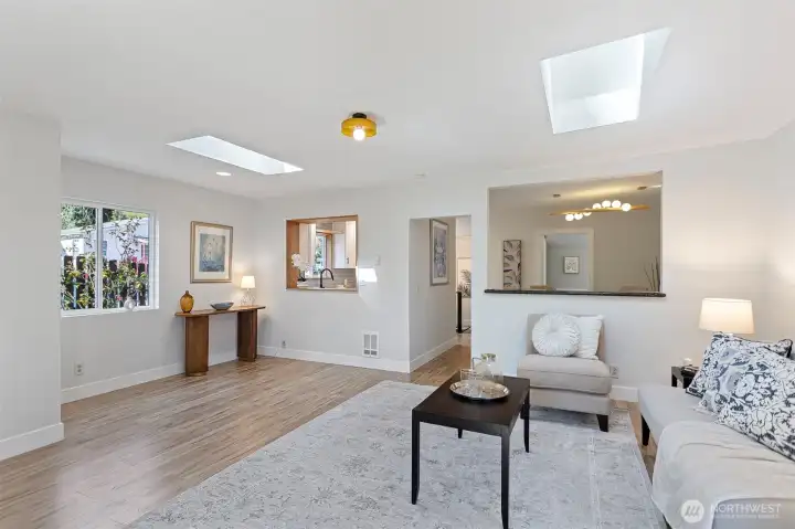 Every opening earns its place: wood-framed serve-through to the kitchen, open-cased passage to the dining room, two skylights overhead. Light moves through this room all day.