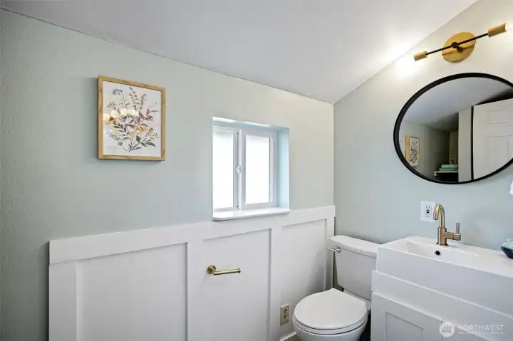 Board-and-batten wainscoting, brass fixtures, round black-framed mirror — the main floor ¾ bath punches above its square footage.