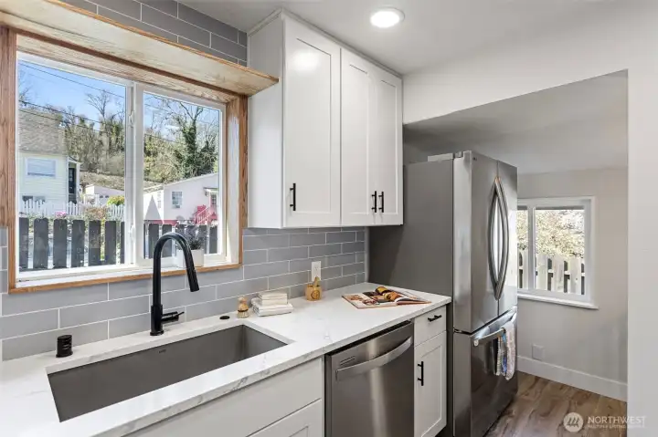 The sink wall: oak-framed west window with sill shelf, matte black faucet, quartz counters. Light lingers here longer than you'd expect.