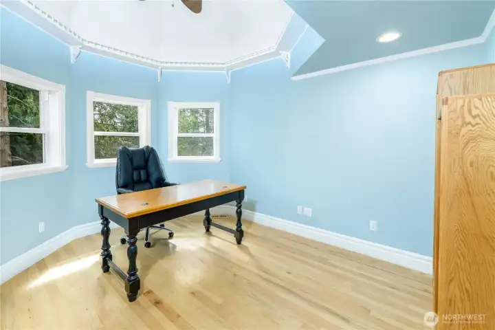 Bright turret-style office or flex room with hardwood floors, high ceilings, recessed lighting, and multiple windows overlooking peaceful evergreen views. Bright turret-style office or flex room with hardwood floors, high ceilings, recessed lighting, and multiple windows overlooking peaceful evergreen views.