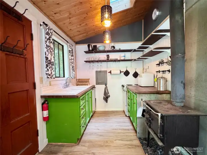 Galley kitchen with wood stove, cute farmhouse sink, oven, and small refrigerator