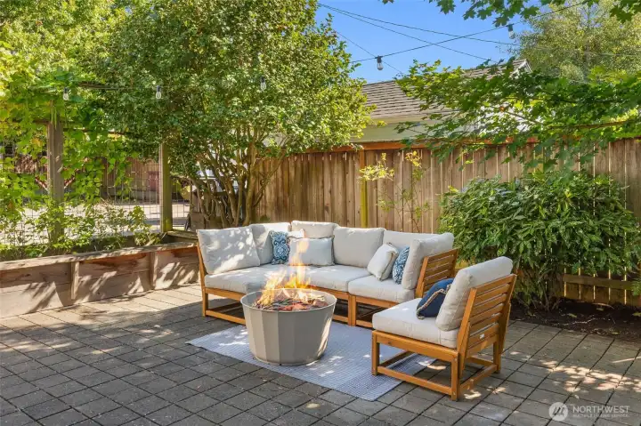 String light lit outdoor room framed by raised beds and evergreen screening.