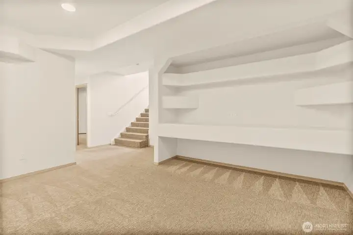 Lower level with built-in storage shelves, carpet, and flexible space for hobbies or media.