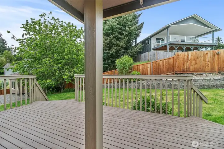Covered back deck overlooking the fully fenced backyard, mature trees, and landscaped outdoor space.