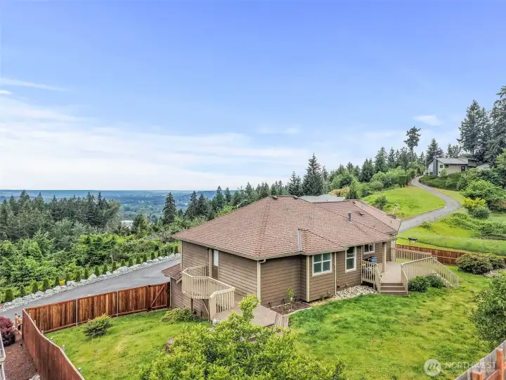 Aerial view of the fully fenced backyard, back decks, mature landscaping, and wide valley views.