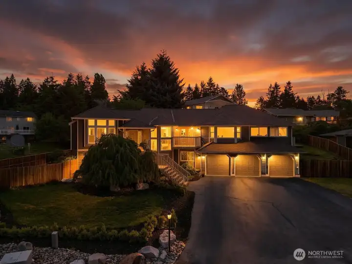 Sunset exterior view with warm lighting, 3-car garage, and mature front landscaping.