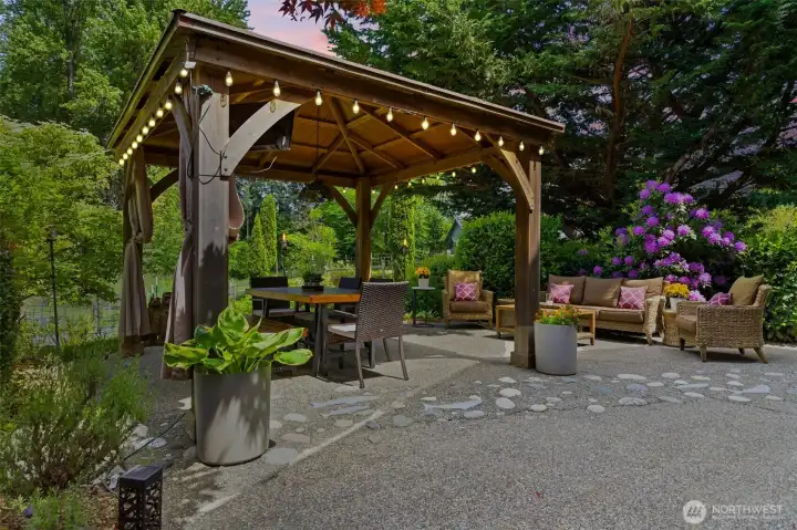 Resort-style outdoor living with a private gazebo, ambient lighting, dining space, TV sitting area, and beautiful surrounding greenery