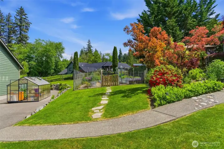 A gardener’s paradise featuring a beautifully enclosed garden area with built-in raised beds, thriving plantings, and a dedicated greenhouse for year-round growing