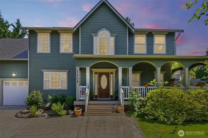 The stunning front elevation showcases timeless architecture, expansive windows, and a beautifully designed wraparound deck that creates unforgettable curb appeal