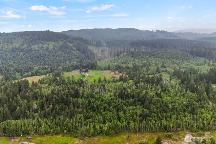 Elevated drone view capturing the surrounding foothills, wooded acreage, and neighboring countryside.