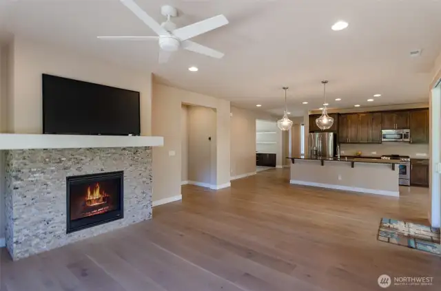 Great room features a beautiful stone faced mantle and fireplace.  Lots of furniture options in this open space.  From this view you can see large kitchen island, primary bedroom to the left and open den ahead.