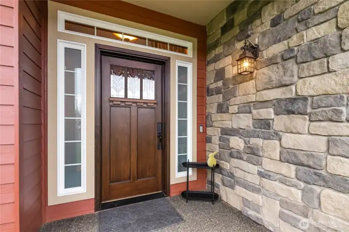 The inviting front porch enhances the home’s Northwest style with stone accents, warm lighting, and striking solid wood door framed by elegant windows.