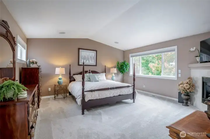 Primary lies under vaulted ceilings, on the plush carpet and beside a primary suite fireplace.