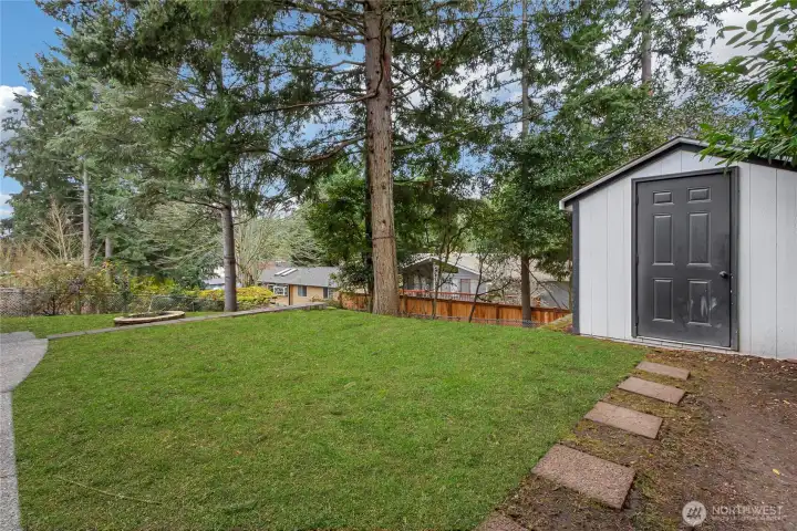 Back yard showing one of two storage sheds, firepit and some trees. (Note that yard/green was virtually enhanced)