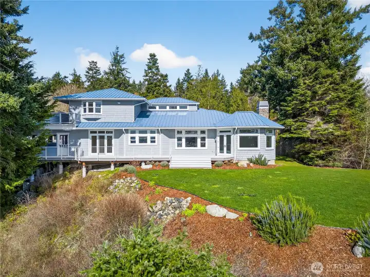 Stunning custom home with a striking metal roof, expansive windows, and beautifully landscaped grounds, perfectly positioned to capture serene views and a peaceful Northwest setting.