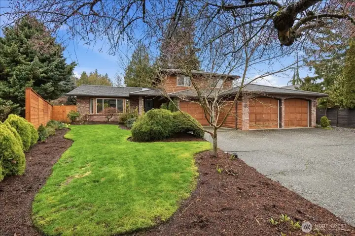 Welcoming front exterior with lush landscaping, metal roof, oversized driveway, and spacious 3-car garage.