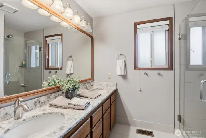 Updated primary bath with dual sinks, quartz counters, tile floors, and a glass-enclosed tile shower.