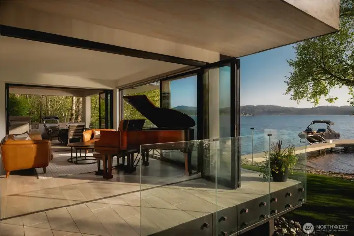 Encased in glass, the architecture remains closely tied to the shoreline, extending toward the covered outdoor lounge beyond.